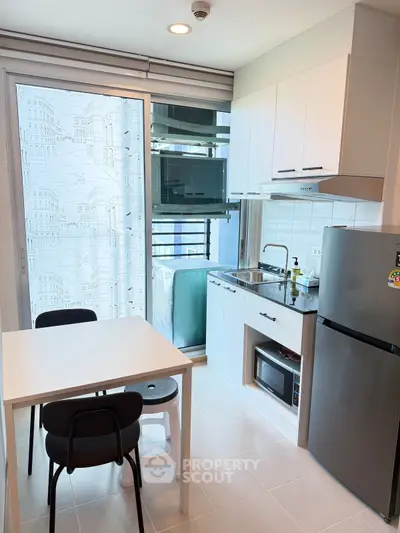 Modern kitchen with dining area, featuring sleek appliances and natural light from large window.