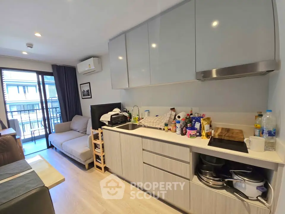 Modern compact living room with open kitchen and balcony view, featuring sleek cabinetry and cozy seating.