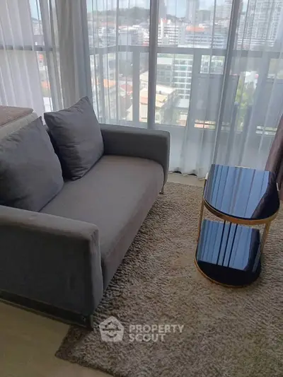 Modern living room with cozy gray sofa and glass table, offering a stunning city view through large windows.