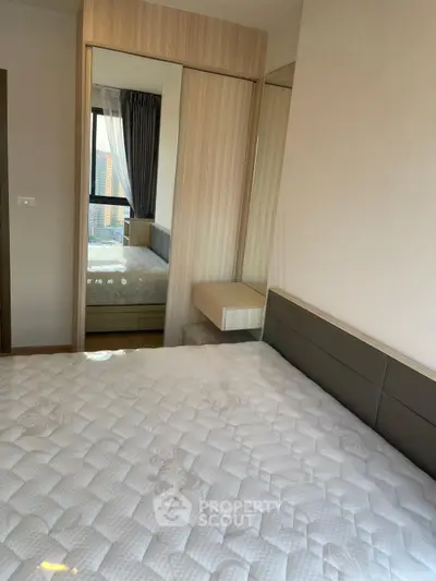 Modern bedroom with large mirror and city view, featuring a comfortable mattress and stylish decor.