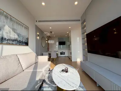 Modern living room with open kitchen, featuring sleek furniture and large wall-mounted TV.