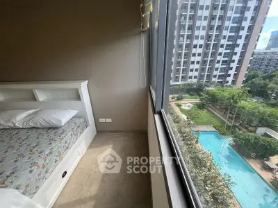 Spacious bedroom with large window offering stunning pool and garden view in modern high-rise building.