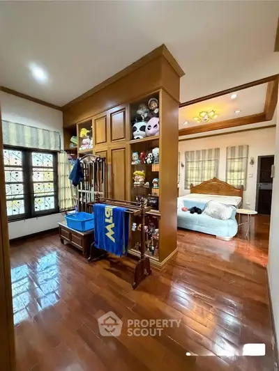 Spacious bedroom with wooden flooring and built-in shelving, featuring a cozy bed and ample natural light.