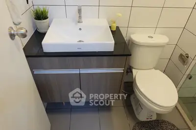 Modern bathroom with sleek sink and toilet, stylish tiles, and decorative plants.