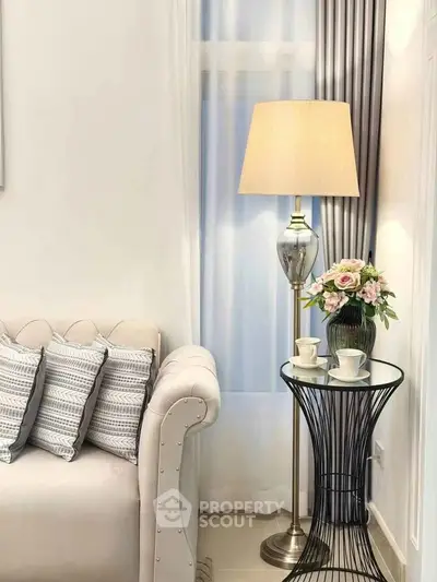 Elegant living room corner with plush sofa, stylish lamp, and chic side table with flowers.