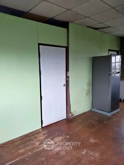 Spacious room with wooden flooring and green walls, featuring a closed door and a refrigerator.