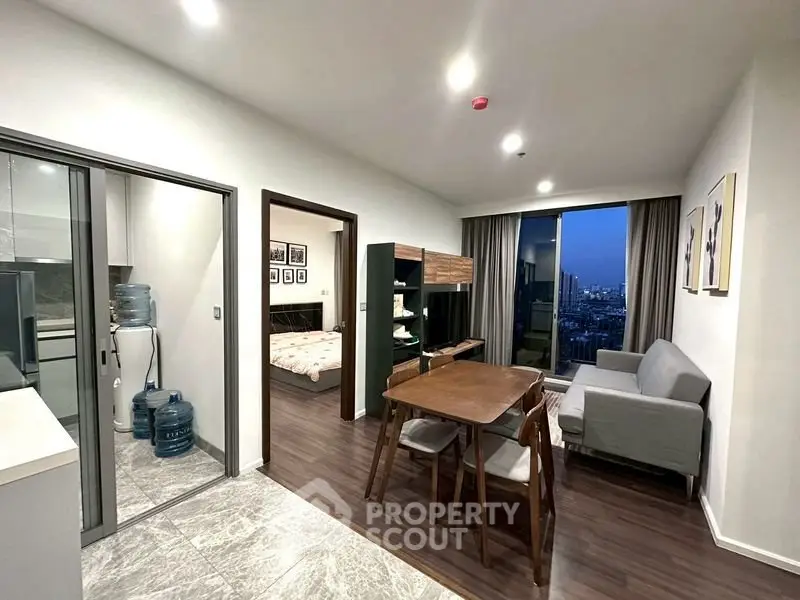 Modern apartment interior with open living and dining area, featuring a city view from the window.