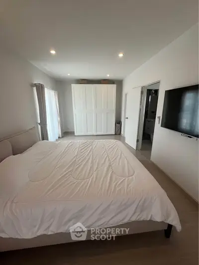 Spacious modern bedroom with large bed, wall-mounted TV, and ample natural light.