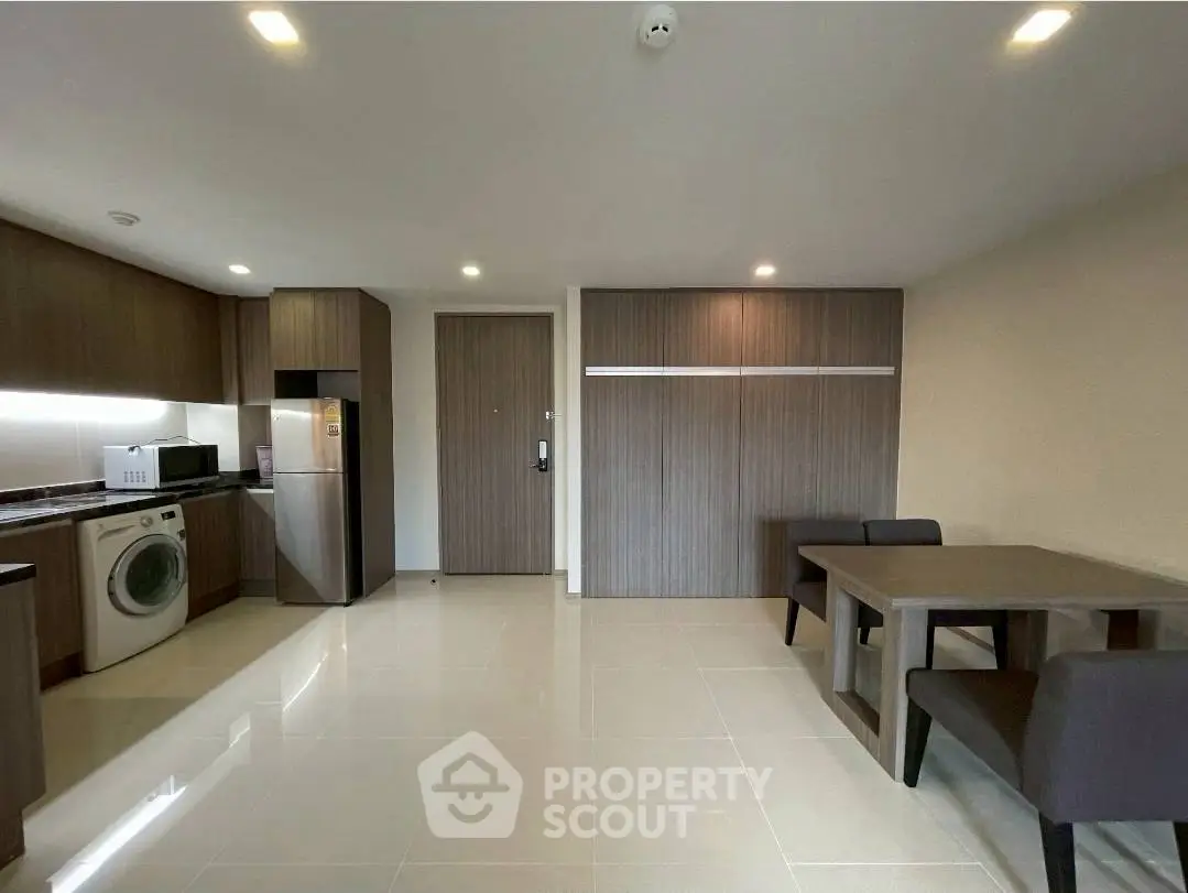 Modern kitchen with sleek cabinetry, washing machine, and dining area in open layout.