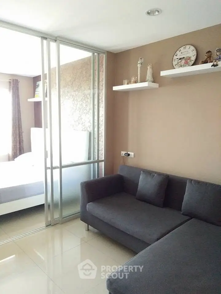 Modern living room with cozy gray sofa and sliding glass doors leading to a bright bedroom.