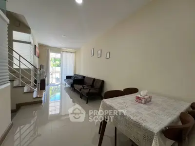 Spacious living room with modern decor and dining area, featuring natural light and elegant staircase.