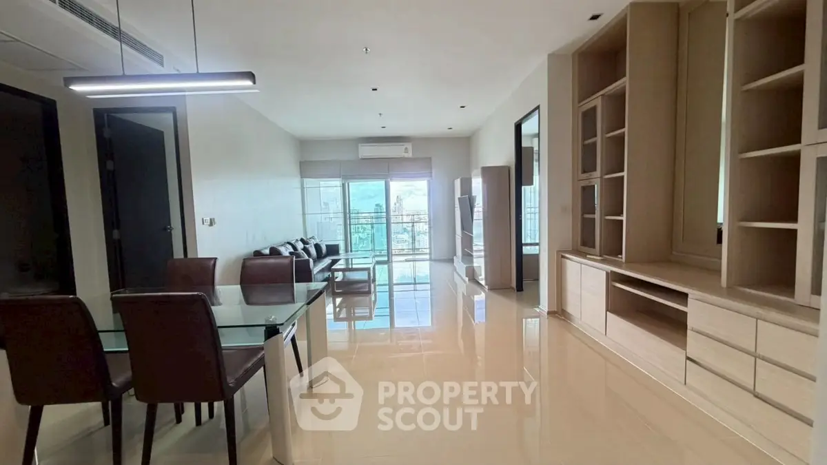 Spacious modern living room with glass dining table and large windows offering city views.