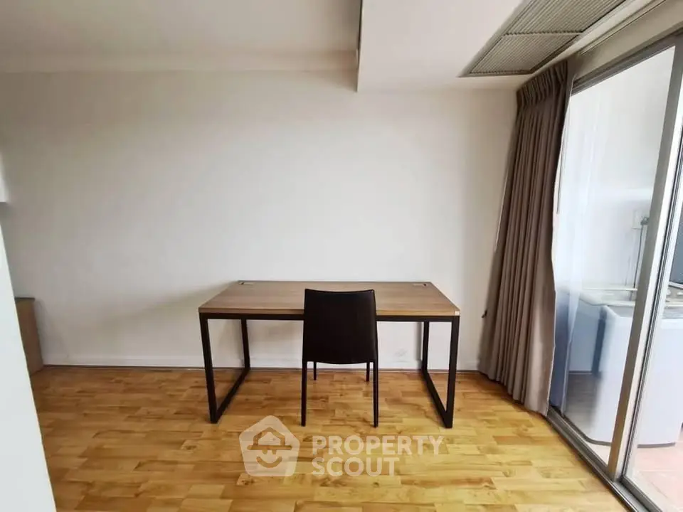 Minimalist study room with wooden desk and chair, sliding glass door to balcony, perfect for productivity.