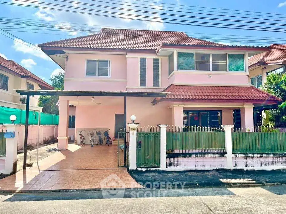 Charming two-story pink house with tiled driveway and green fence in a sunny neighborhood.
