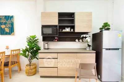 Modern kitchen with sleek cabinetry, dining area, and stainless steel fridge in a cozy apartment.