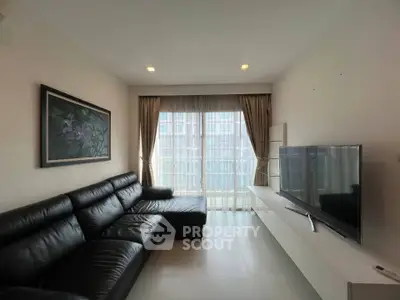 Modern living room with sleek black leather sofa and large TV, featuring floor-to-ceiling windows.