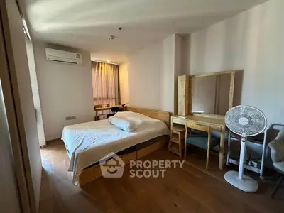 Spacious bedroom with wooden flooring, featuring a bed, desk, and air conditioning.