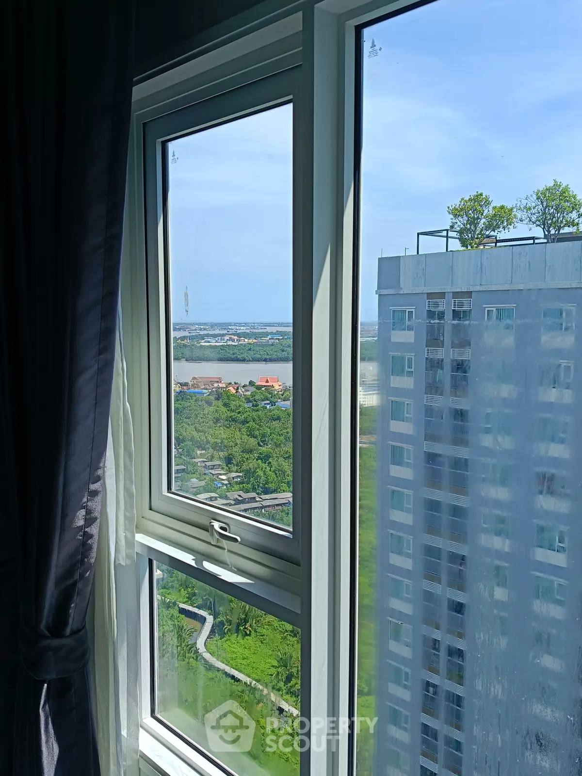 Stunning high-rise apartment window view with lush greenery and distant water scenery.