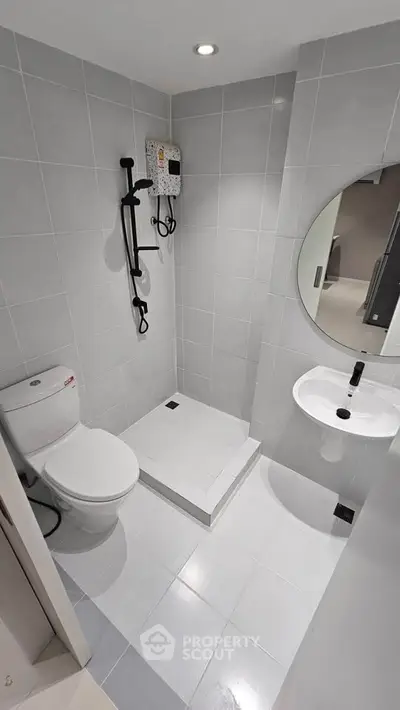 Modern bathroom with sleek design, featuring a round mirror, shower, and white fixtures.