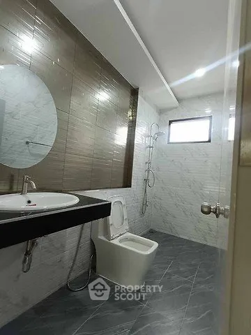 Modern bathroom with sleek design, featuring a round mirror, stylish tiles, and a spacious shower area.