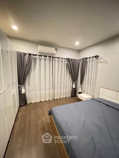 Modern bedroom with sleek design, featuring large windows and elegant curtains for a cozy ambiance.