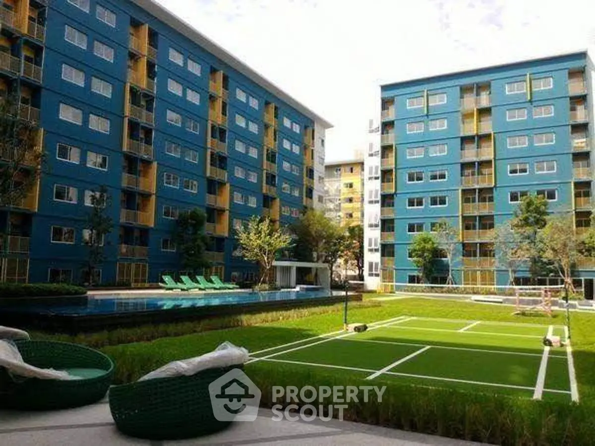 Modern apartment complex with tennis court and pool, vibrant blue buildings, lush greenery, and inviting outdoor amenities.