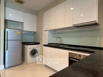 Modern kitchen with sleek cabinetry, washing machine, and built-in oven in a stylish apartment.