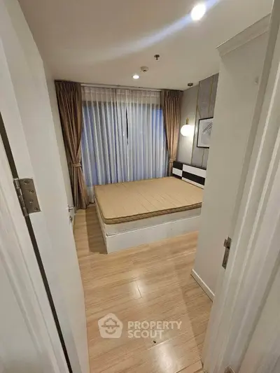 Cozy bedroom with wooden flooring and large window draped with curtains, perfect for relaxation.