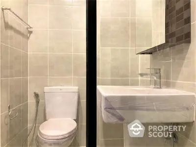 Pristine bathroom with modern fixtures, neutral tiles, and a sleek wall-mounted sink, showcasing a clean and functional design ideal for contemporary living.