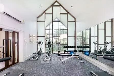 Spacious modern gym with high ceilings and large windows in luxury real estate property.