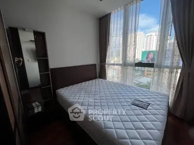 Spacious bedroom with large window offering city views, featuring a comfortable bed and elegant curtains.