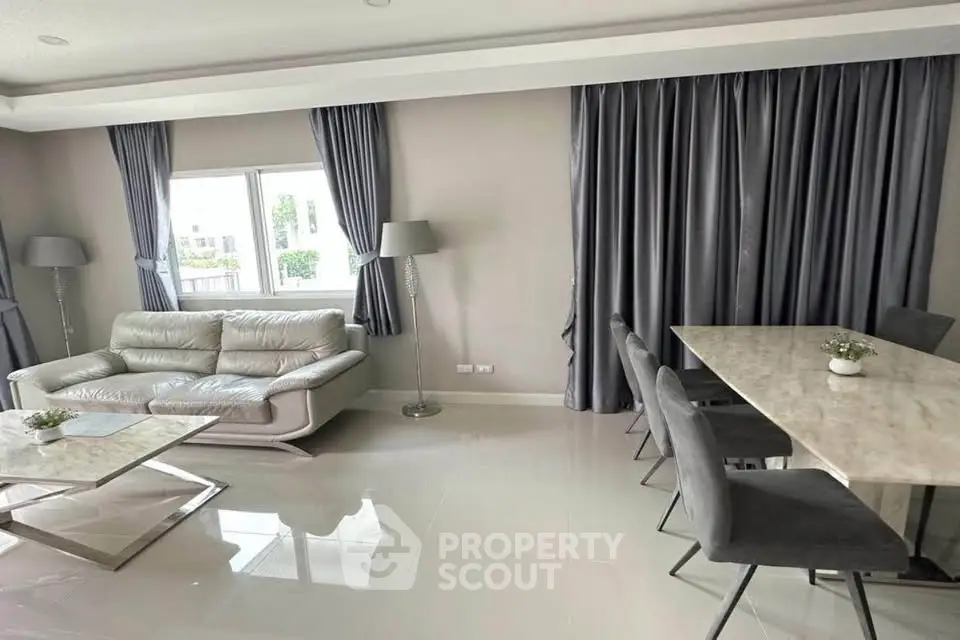 Modern living room with sleek furniture and elegant dining area, featuring large windows and stylish decor.