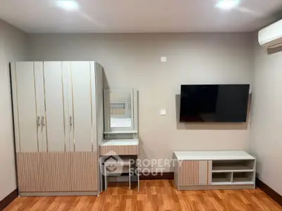 Modern bedroom with sleek wardrobe, vanity, and wall-mounted TV on wooden flooring.