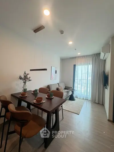 Modern living room with dining area, stylish furniture, and natural light from large window.
