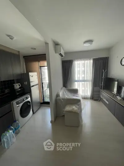Modern living room with kitchen, featuring washing machine and TV, in a cozy apartment.