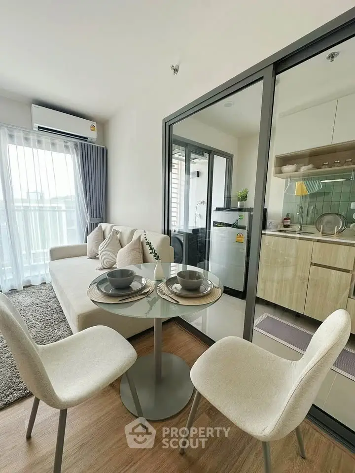 Modern living room with open kitchen and balcony view, featuring stylish furniture and natural light.