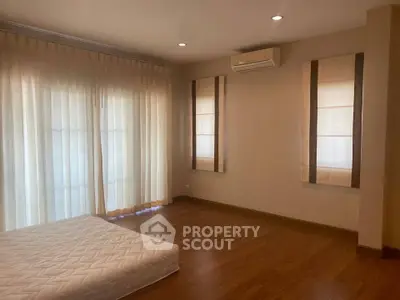 Spacious bedroom with wooden flooring and natural light, featuring a minimalist design and air conditioning.