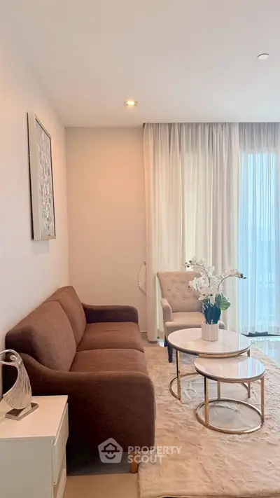 Elegant living room with plush sofa, chic armchair, and stylish coffee tables by large window.