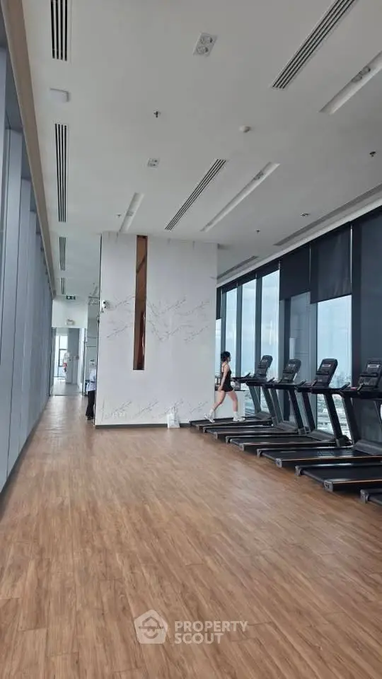 Modern gym with treadmills and floor-to-ceiling windows in a high-rise building.