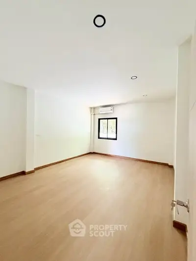Spacious empty room with wooden flooring and natural light, ideal for customization.