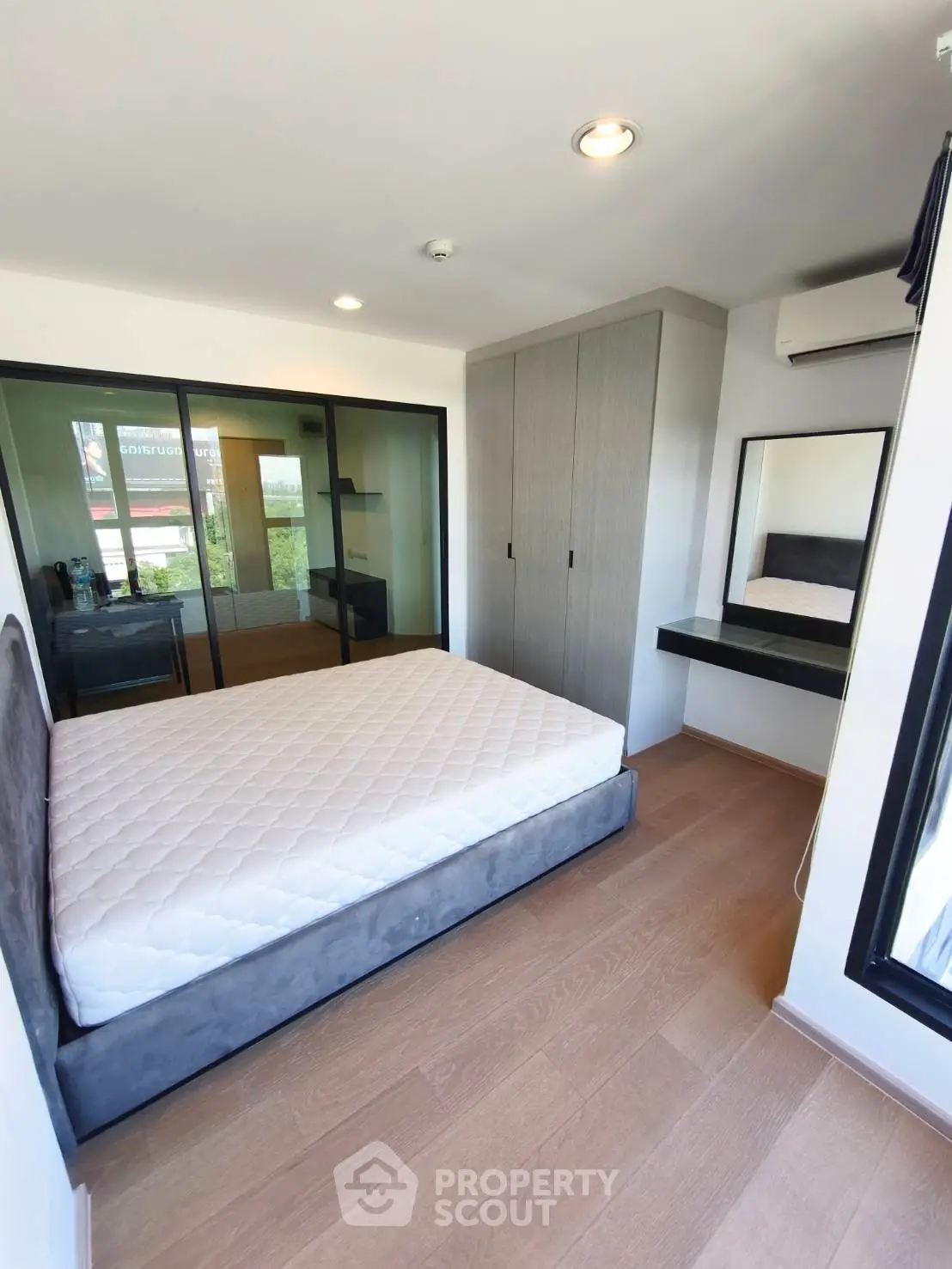Modern bedroom with large window, built-in wardrobe, and hardwood floors in a stylish apartment.