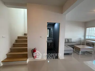 Modern living room with staircase and adjacent bathroom, featuring sleek furniture and natural light.