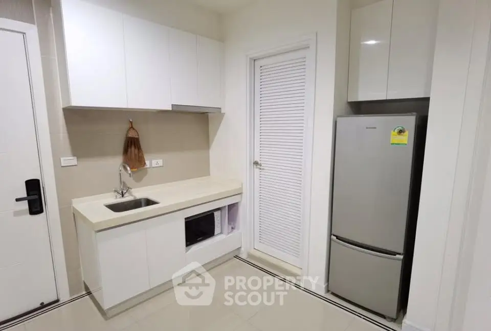 Modern kitchen with sleek cabinetry and stainless steel fridge in a compact layout.