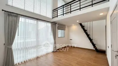 Spacious modern living room with high ceiling and mezzanine, featuring large windows and elegant curtains.