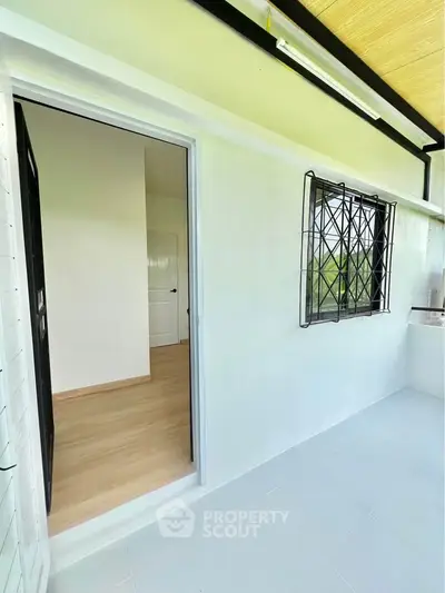 Bright balcony with open door leading to interior space, featuring secure window grill.