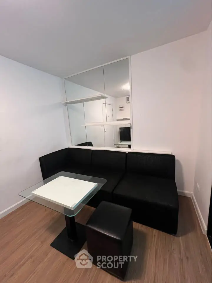 Modern living room with sleek black sofa and glass table, featuring minimalist design and wooden flooring.