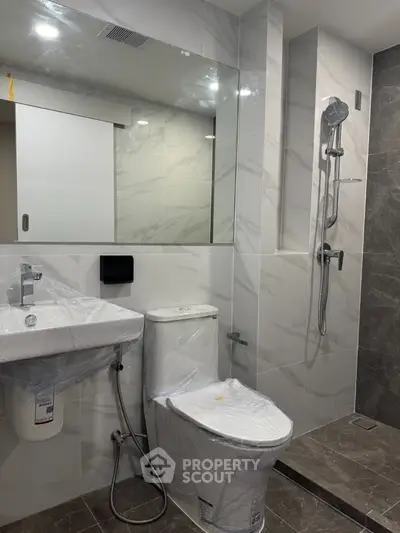 Modern bathroom with sleek fixtures and marble tiles, featuring a shower and toilet.