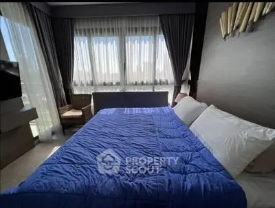 Modern bedroom with blue bedding and large windows offering natural light.