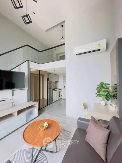 Modern living room with high ceiling and mezzanine, featuring sleek furniture and air conditioning.