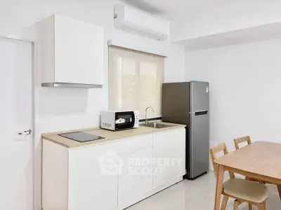 Modern kitchen with sleek white cabinetry, stainless steel fridge, and dining area.